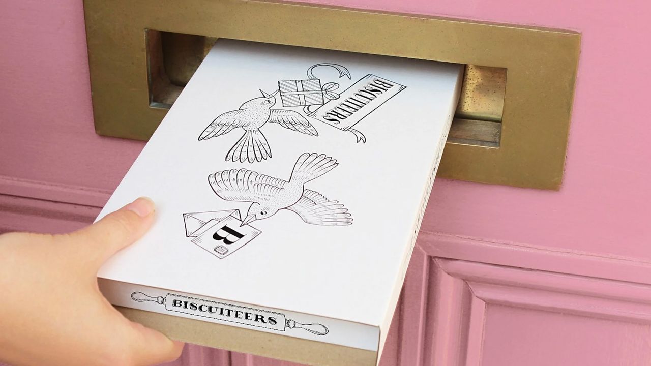 Valentine&#039;s Day gifts: Biscuiteers box being posted through letterbox of pink dor