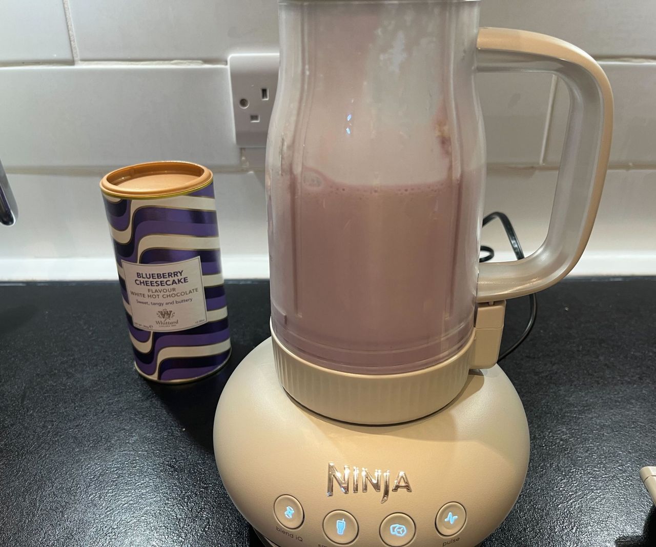 A blended blueberry milkshake inside a tumbler blender on a black kitchen counter.