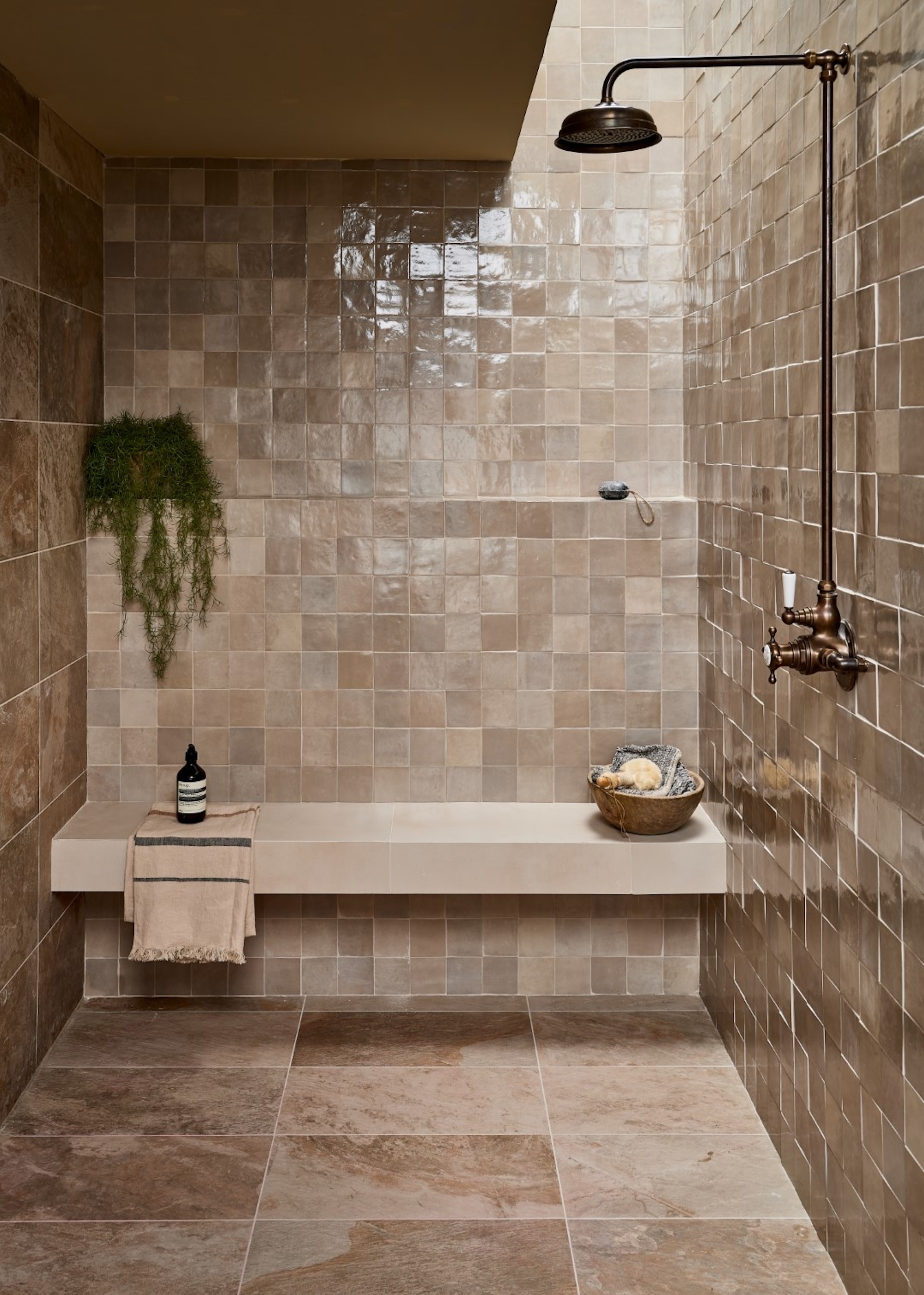 a walk in shower clad in warm taupe colored tiles with a gentle finish, a built in shower bench and large shower rose