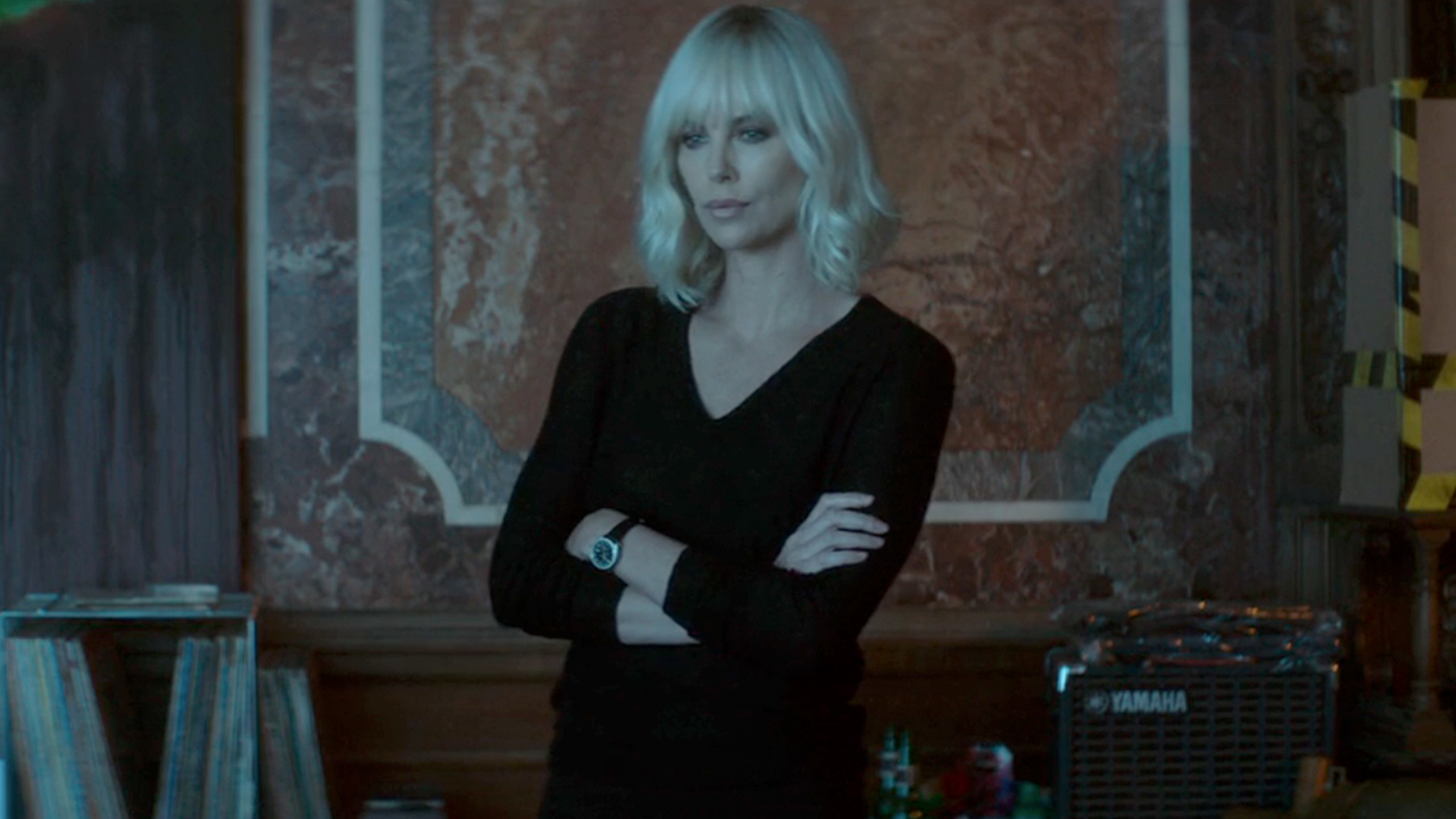 Charlize Theron in a black dress, with her arms crossed in Atomic Blonde