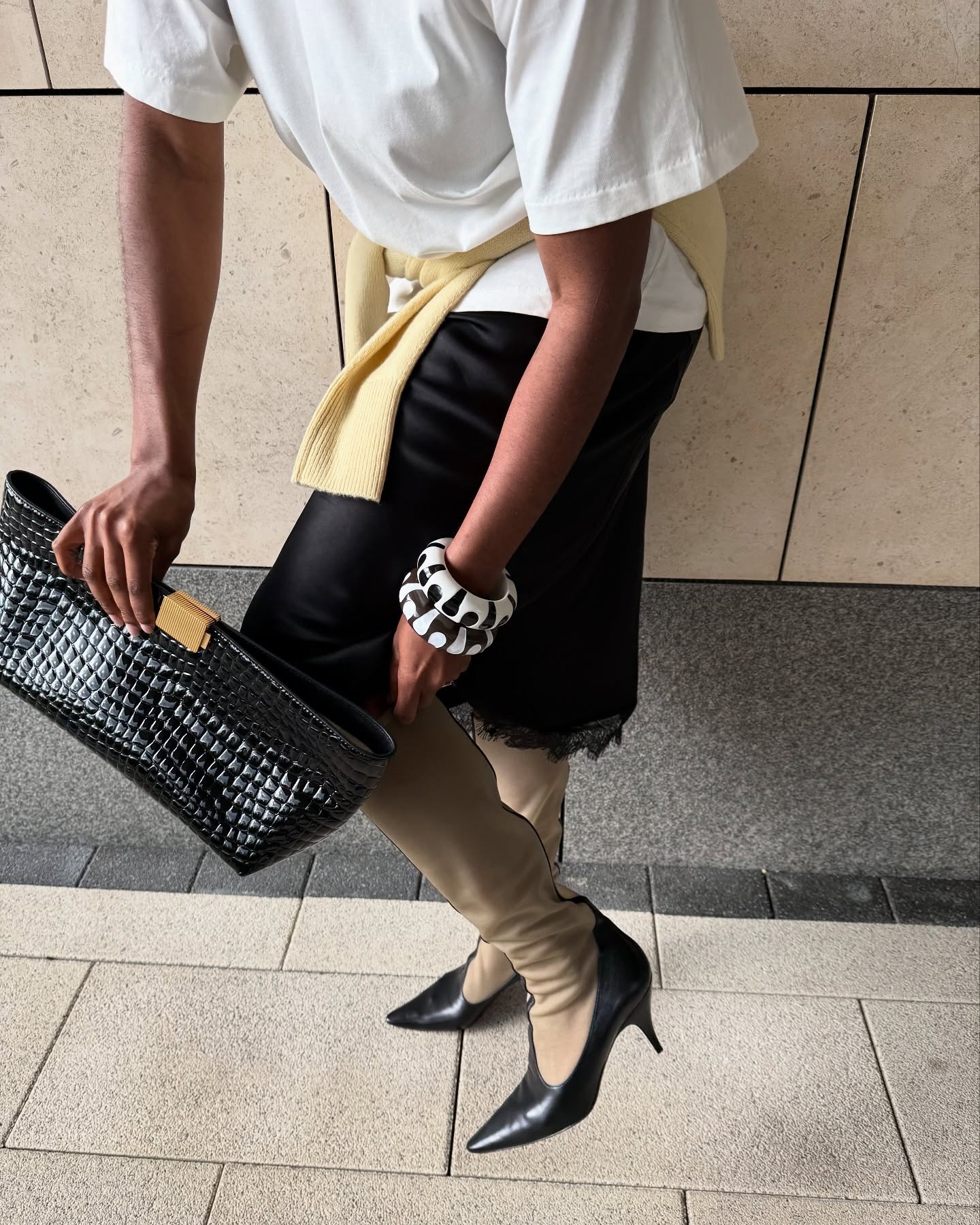 A woman wearing a white oversized tee, yellow sweater tied on her waist, a black lace-trim slip skirt, and black and white bangles.