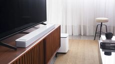 Bose 900 soundbar on dark wood cabinet placed in front of TV, with subwoofer on the floor beside