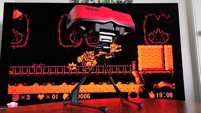 Virtual Boy for Switch 2 sitting on coffee table with TV in backdrop displaying Wario Land gameplay.