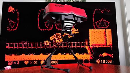 Virtual Boy for Switch 2 sitting on coffee table with TV in backdrop displaying Wario Land gameplay.