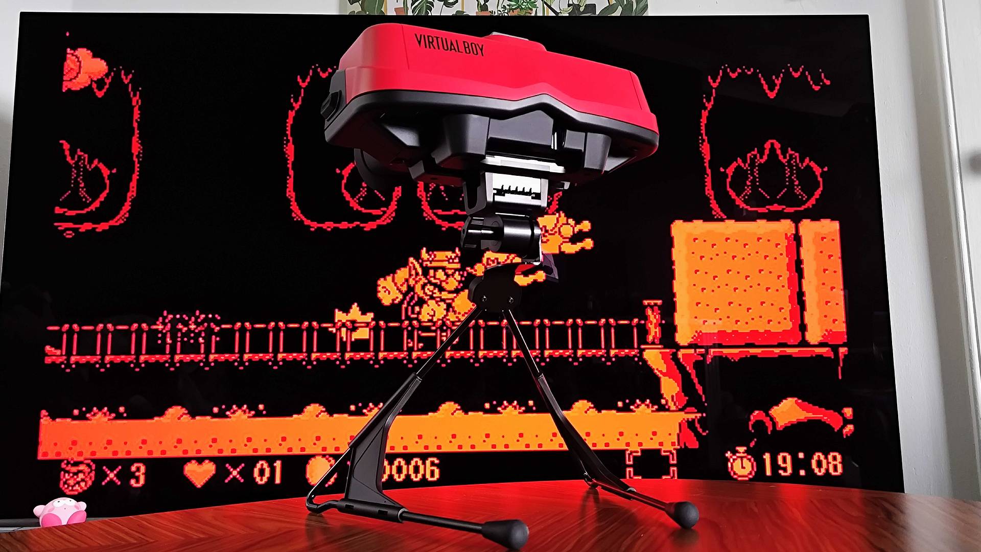 Virtual Boy for Switch 2 sitting on coffee table with TV in backdrop displaying Wario Land gameplay.