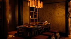 An atmospheric bar reception with a vintage wood desk, red leather and fabric stools, a pendant lamp in tempered squares of golden glass, and a mural depicting a woman stretching on her back nude.