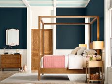Bedroom with navy walls, wooden furniture, and a coral throw blanket on the end of the bed