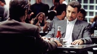 Robert De Niro as Neil McCauley sitting in a restaurant during the '90s thriller movie Heat.