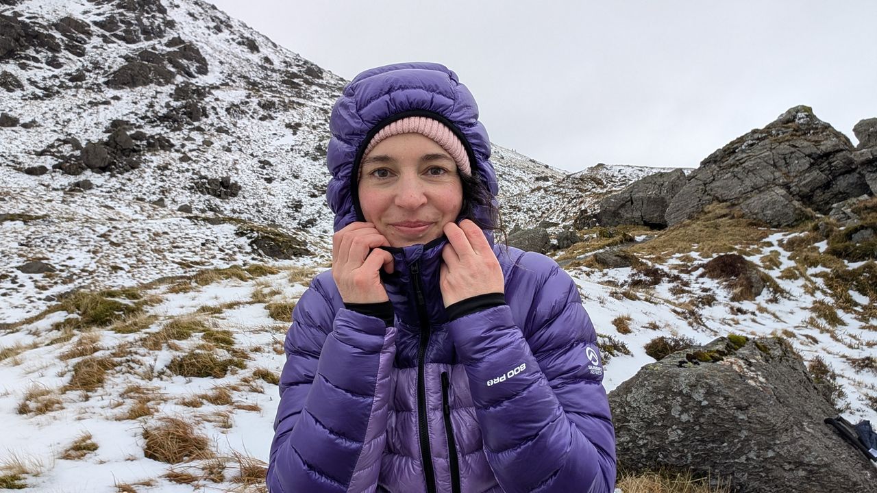 A woman hiker putting her hood up on purple North Face Summit Breithorn Down Jacket