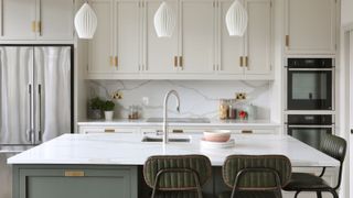 A kitchen with a quartz topped island, a silver fridge in the background and a chrome tap in the centre of the image over an undermount sink