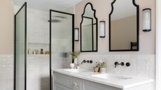 A bathroom with a double vanity unit, two black framed mirrors, and a shower with black framed panels and fluted glass