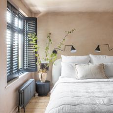 Boho style bedroom with bare plaster walls and modern black wall lights, shutters and window frames