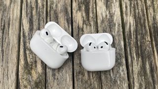 The AirPods 4 and AirPods Pro 2 side by side in their charging cases on a wooden surface.