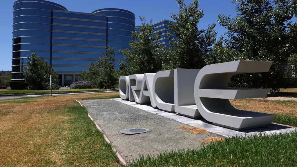 A side on photo of an Oracle sign on a lawn in front of a large blue-glass building