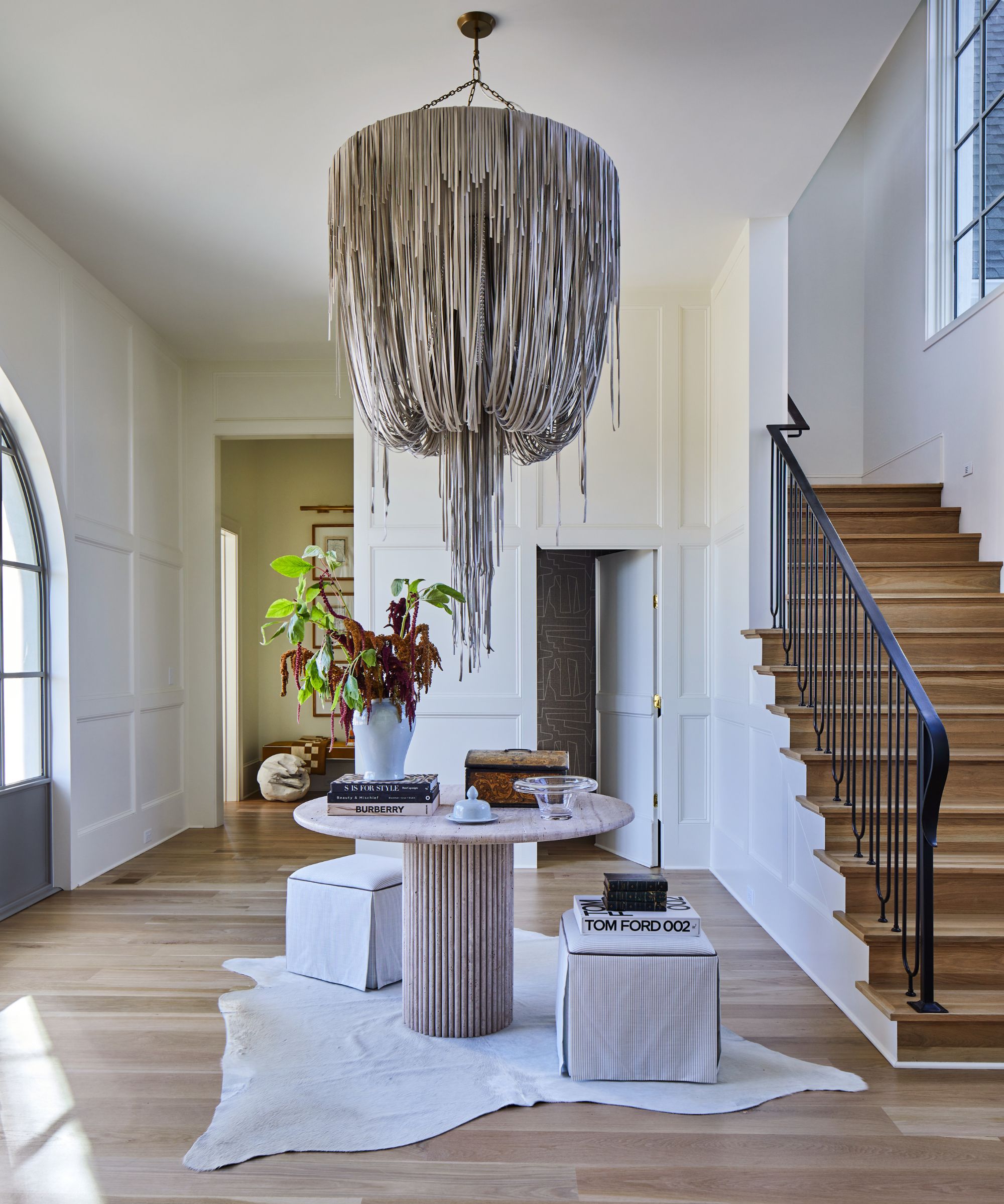 Large white entryway with a marble table in the center and a large modern chandelier hanging above
