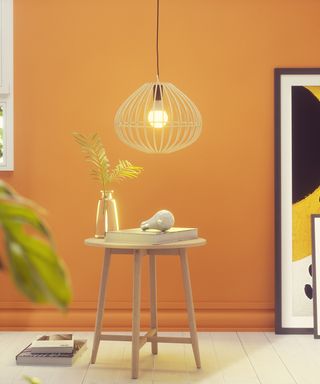 Statement lighting pendant shown in front of an orange wall and side table