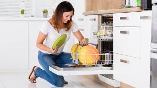 A woman kneeling and loading plates into a dishwasher