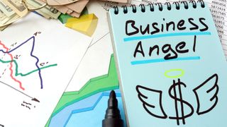 A close up of various papers spread across a desk, including a notepad with the words 'business angel'