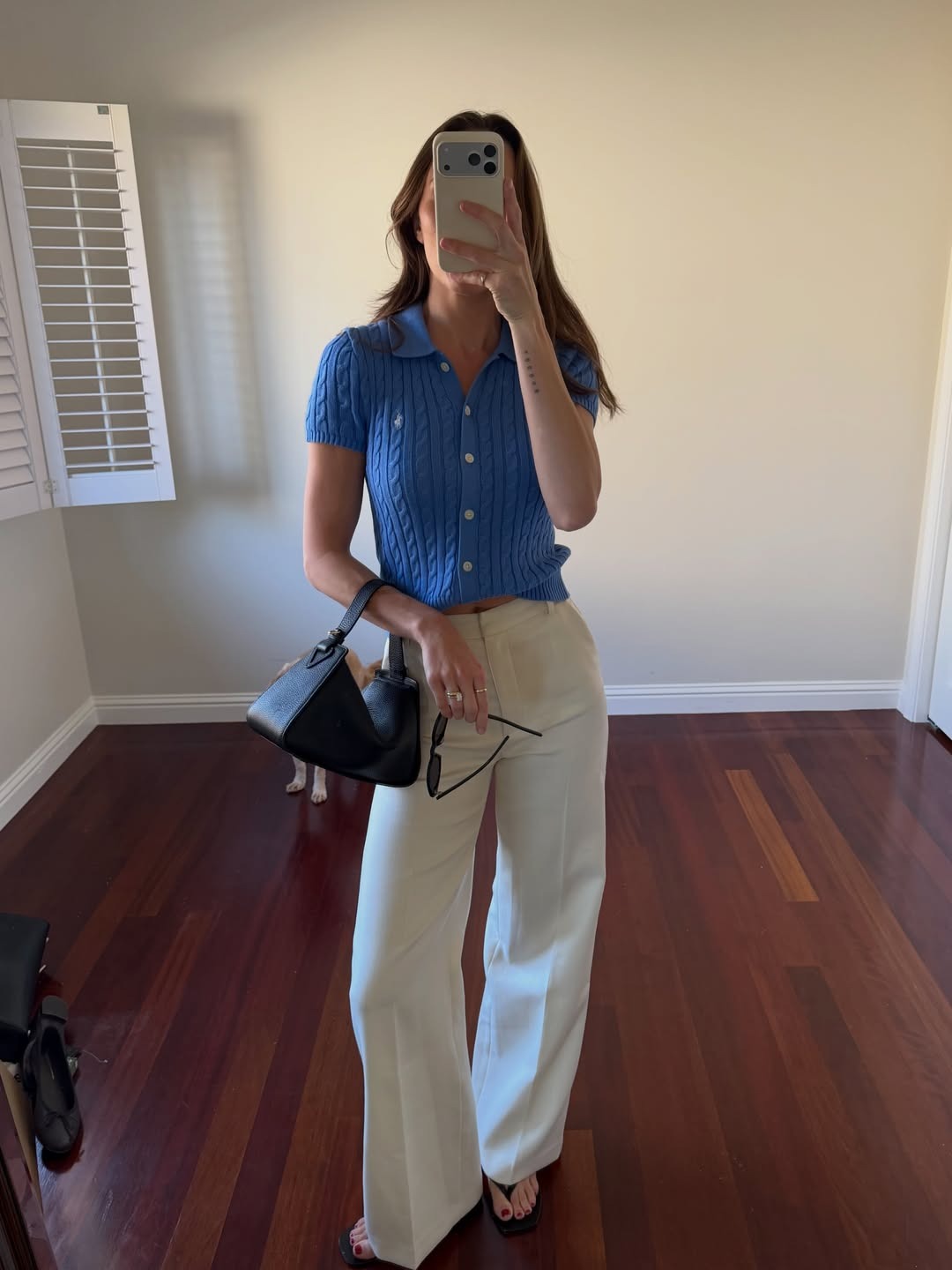 Woman wears blue knit top, white trousers and carries The Horse Clementine bag