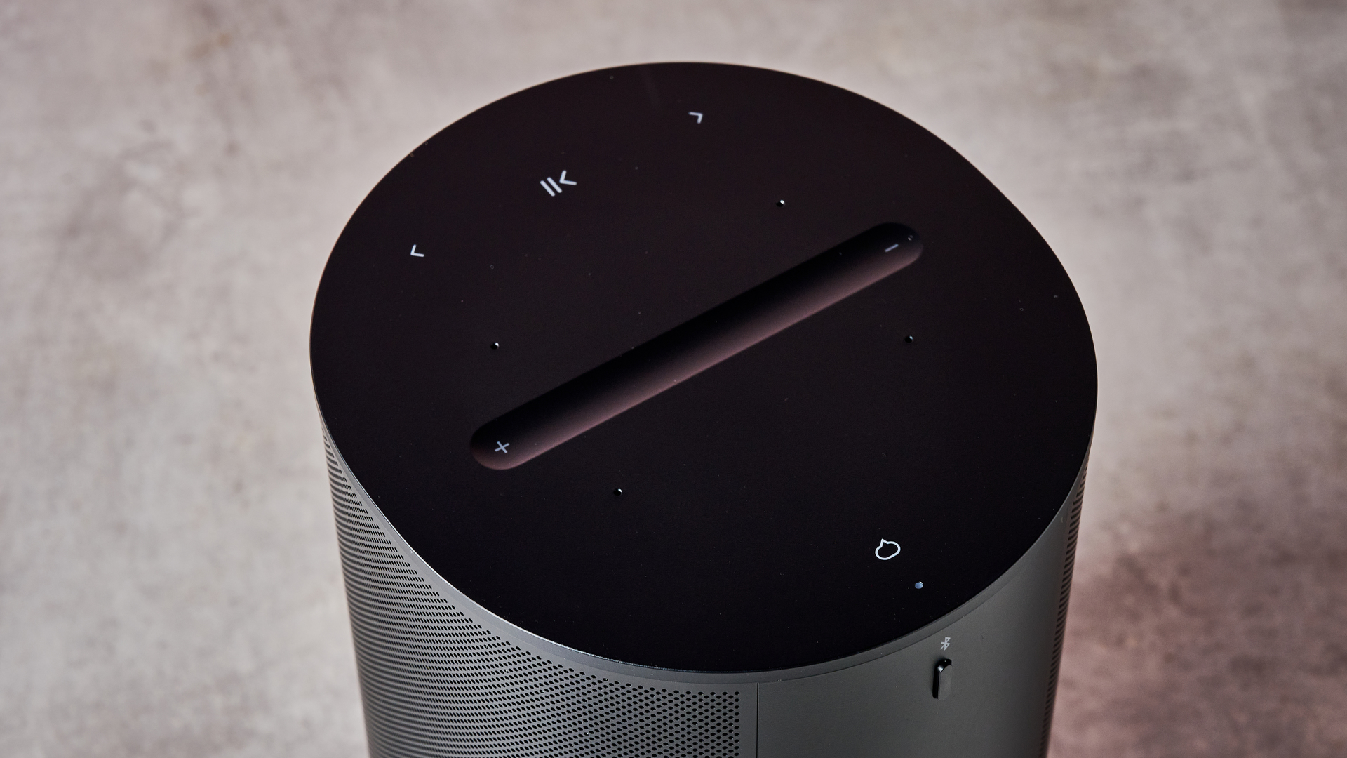 A closeup of the top of the Sonos Era 100, showing its play / pause, skip, volume and mic buttons.