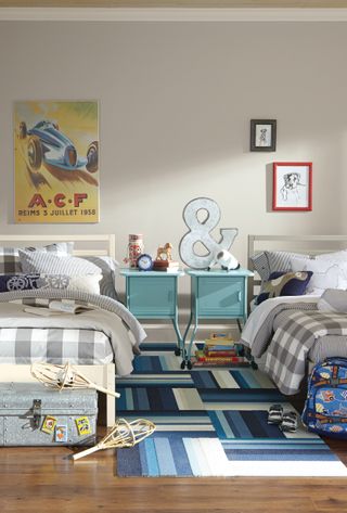 Blue and gray kids shared bedroom with plenty of patterns including gray check bedlinen, pale blue bedside cabinets and colorful wall art.