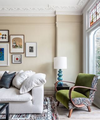 living room with cream sofa, beige painted walls, framed gallery wall, dark wood and green curvaceous lounge chair, blue and white table lamp