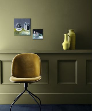 olive green walls with panelled lower half, mustard chair and yellow vases on ledge with two pieces of artwork displayed