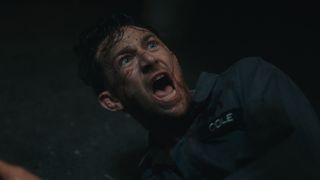 A man with a bloody face lies on the floor and screams at something off-camera