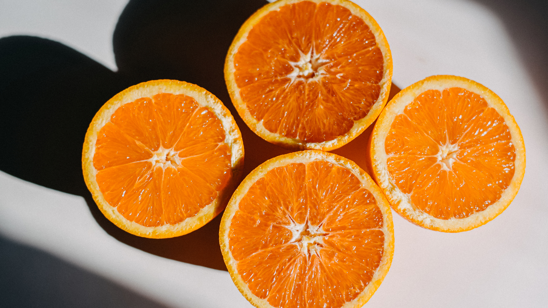 wo naranjas en mitades que proyectan una sombra sobre una superficie blanca.