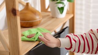 Dusting wooden shelf with damp microfiber cloth