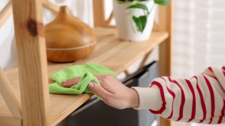 Dusting wooden shelf with damp microfiber cloth