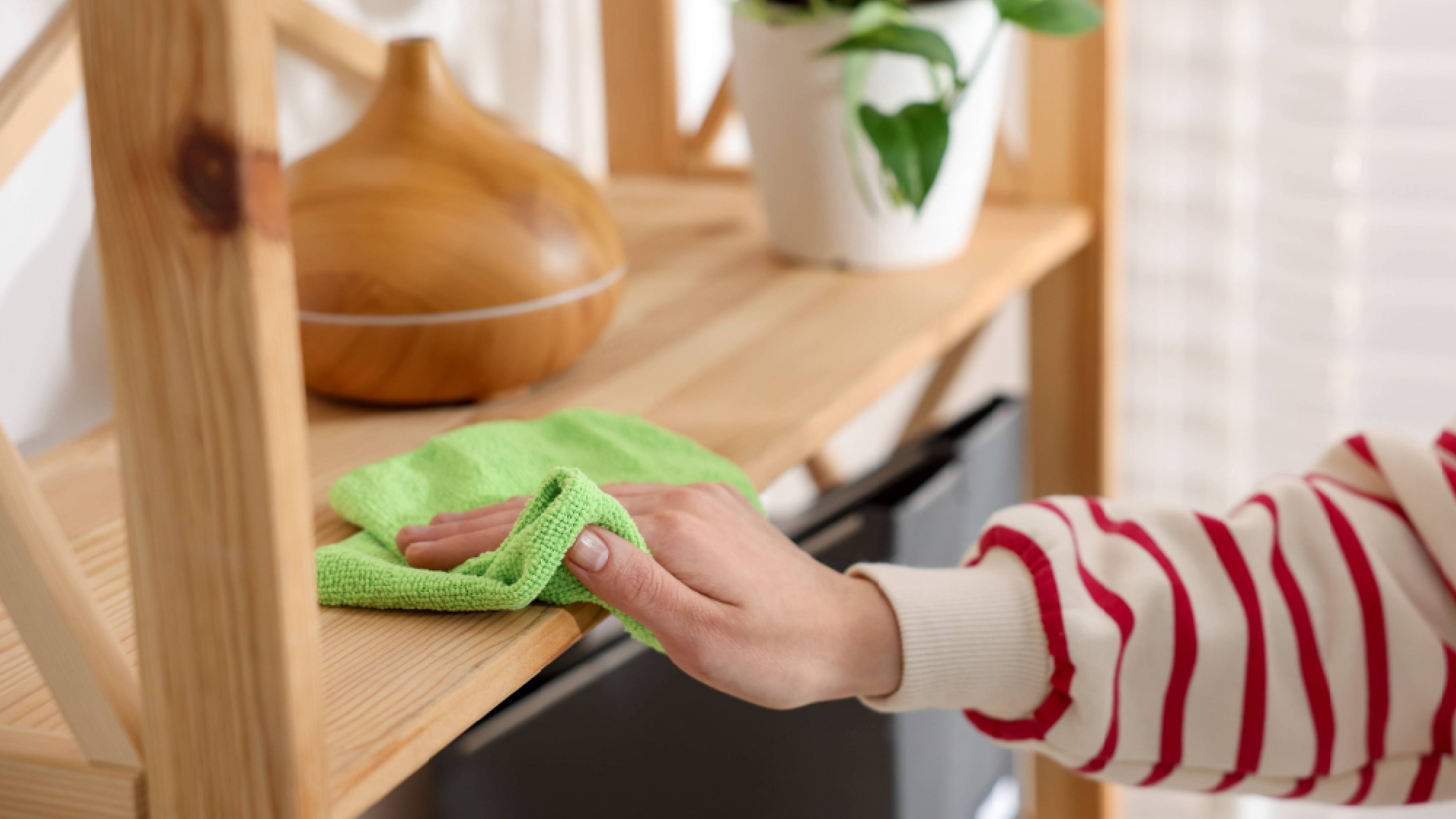 Dusting wooden shelf with damp microfiber cloth