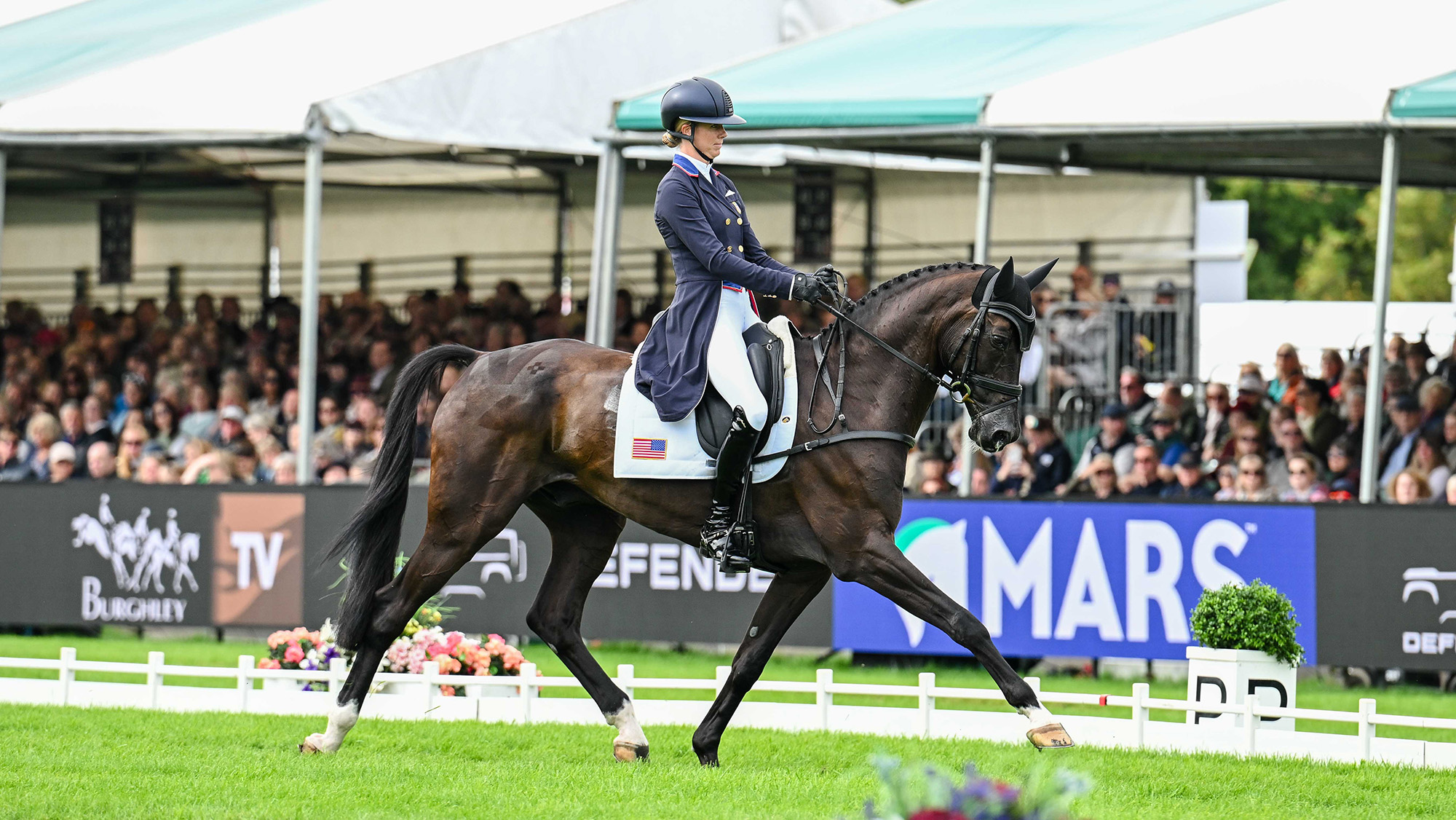 Caroline Pamukcu, a US rider in a blue tailcoat, rides black horse HSH Blake in the Burghley dressage arena on the grass