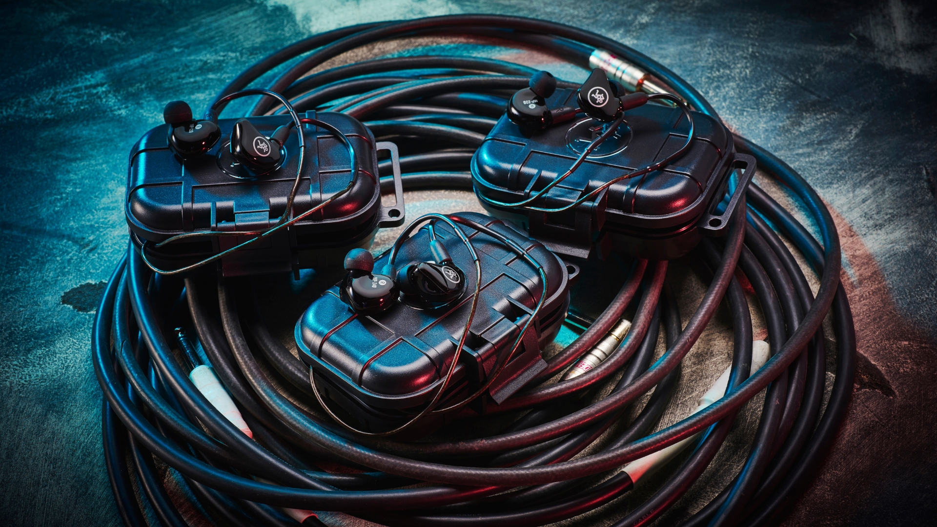 Three pairs of in-ear monitors and their cases lying on top of a bundle of instrument cables