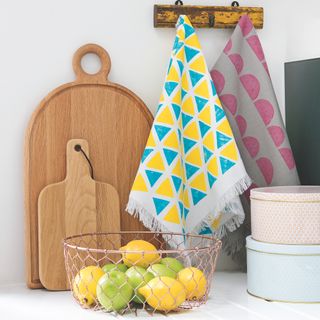 tea towels on hooks with breadboards and bowl of fruit in a kitchen