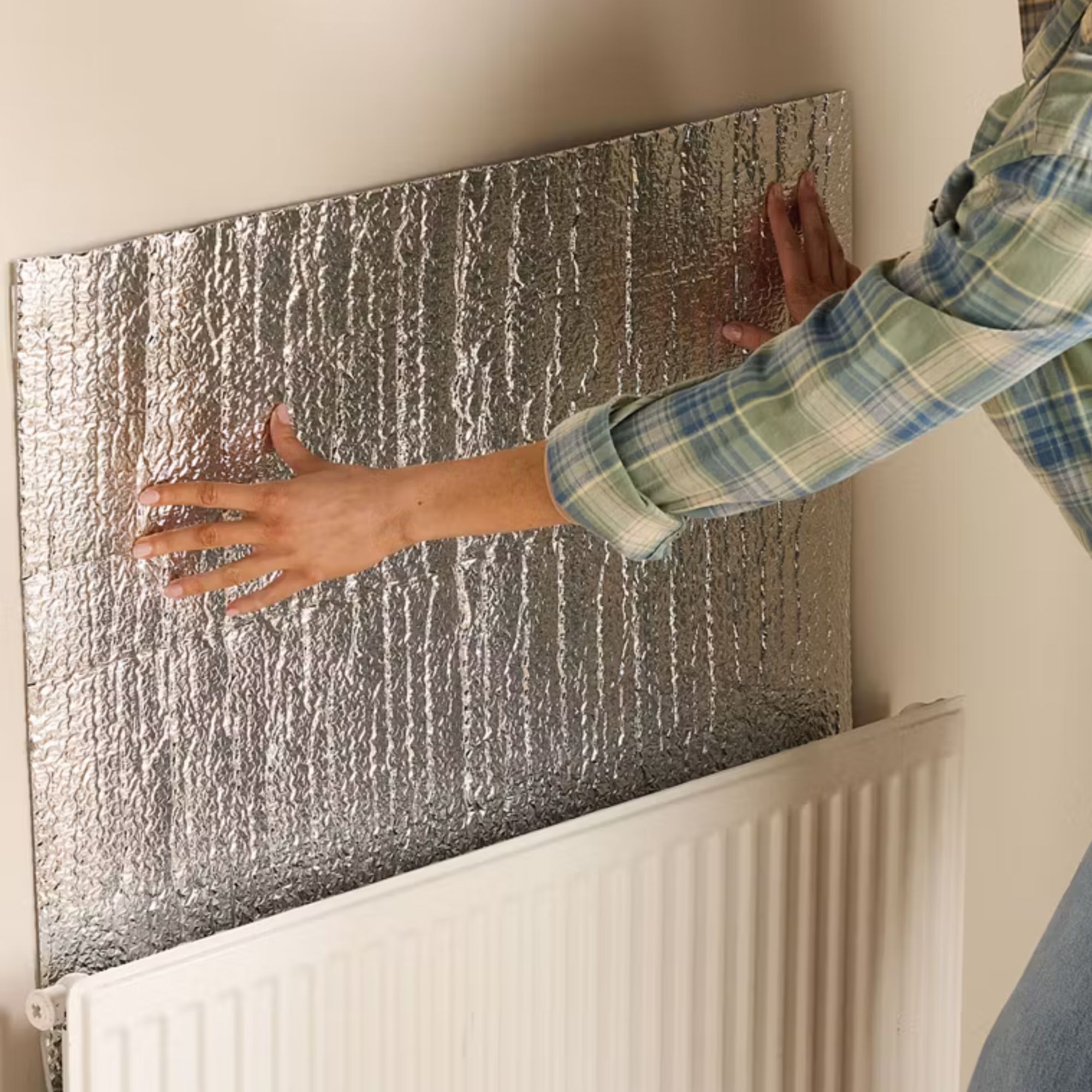 Hands holding radiator foil up above a radiator on white walls
