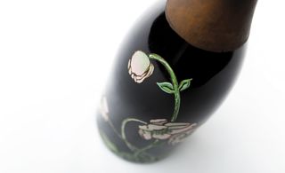 Black champagne bottle decorated with white flowers with green stems painting, and bronze coloured neck, white background