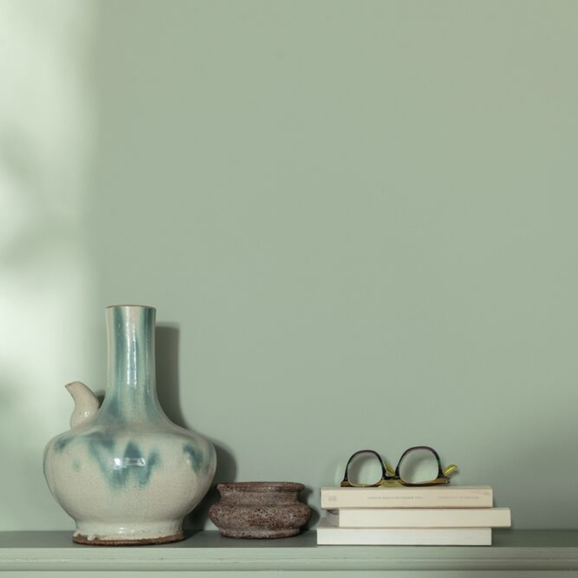 A wall painted in Dulux's Soulful Sage with a few decorative objects displayed on a tonal shelf