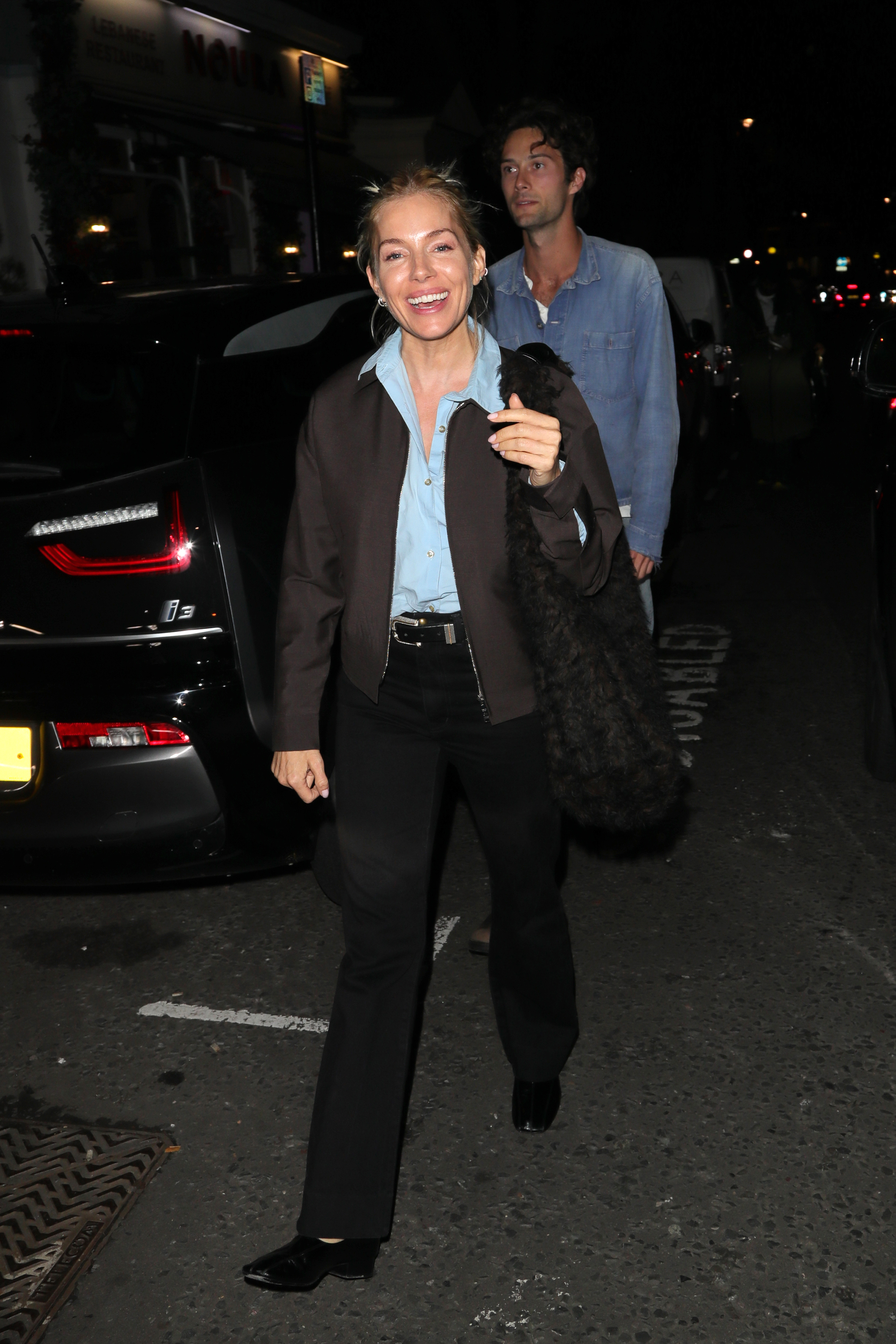 Sienna Miller steps out in London wearing black jeans with square-toe flats, a blue shirt and a dark brown jacket.