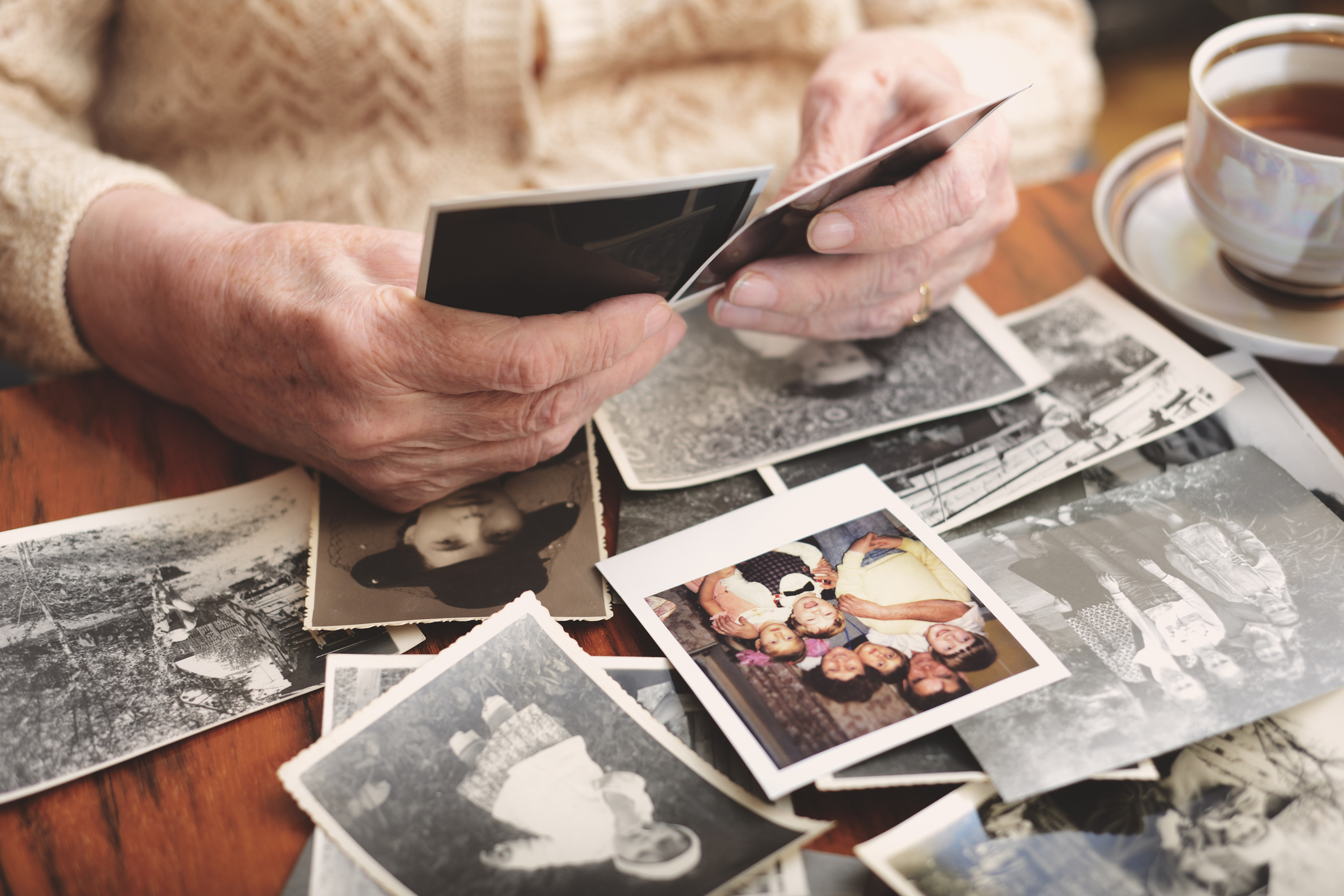 Senior woman sitting at table, looking through old photographs, mid section.