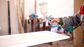 Person using airless spray to add lacquer to kitchen cabinet door