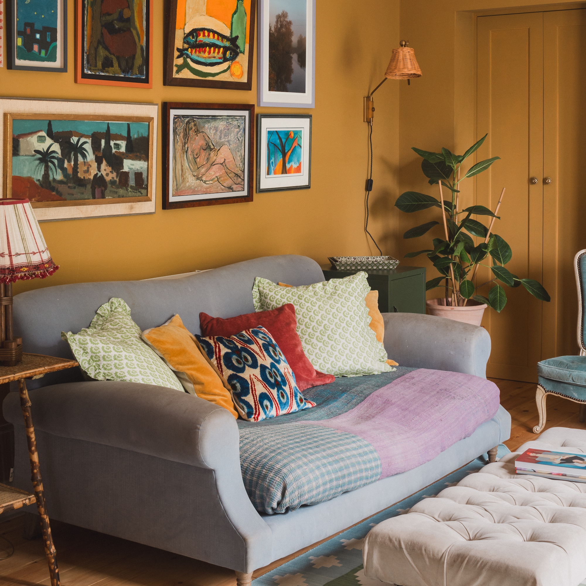 living room with rich yellow walls hung with paintings with grey sofa with bright cushions