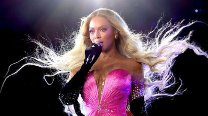 Beyonce wears a pink strapless dress with a low-cut V-neckline, with long black gloves, and her blonde wavy hair blows in the air