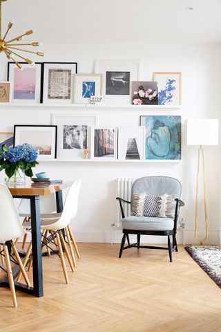 A corner of the open plan kitchen diner with grey and black armchair, shallow shelves filled with artwork, and a floor lamp