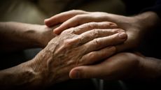 Close-up on the hands of a younger person holding an older person's hands