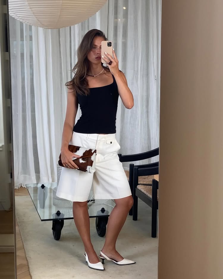 Summer Outfit Ideas 2025: @johannalager wears a pair of white denim Bermuda shorts with a black top and cow-print bag