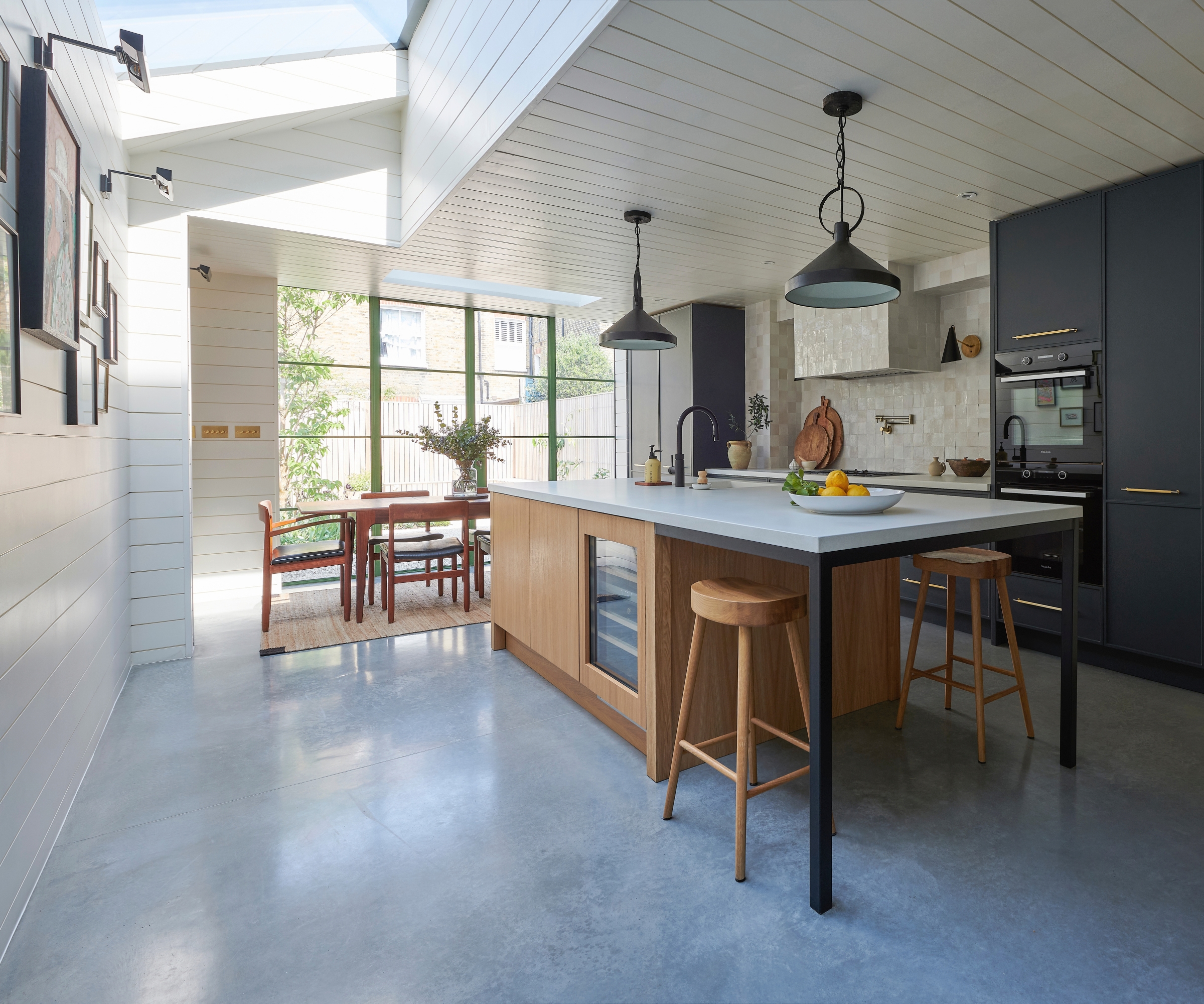 Open-plan kitchen with concrete floors, a wood island with bar stools, black cabinetry, and skylights.