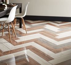 Nayara Floor Tiles wood-effect porcelain tiles in a herringbone pattern using different shades of brown, with a table and chairs to the left of the image