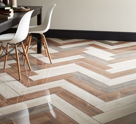 Nayara Floor Tiles wood-effect porcelain tiles in a herringbone pattern using different shades of brown, with a table and chairs to the left of the image