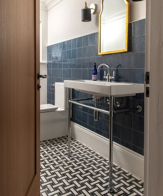 Bathroom with navy blue square wall tiles, basketweave floor tiles, trad basin, gold mirrror, wall lights,